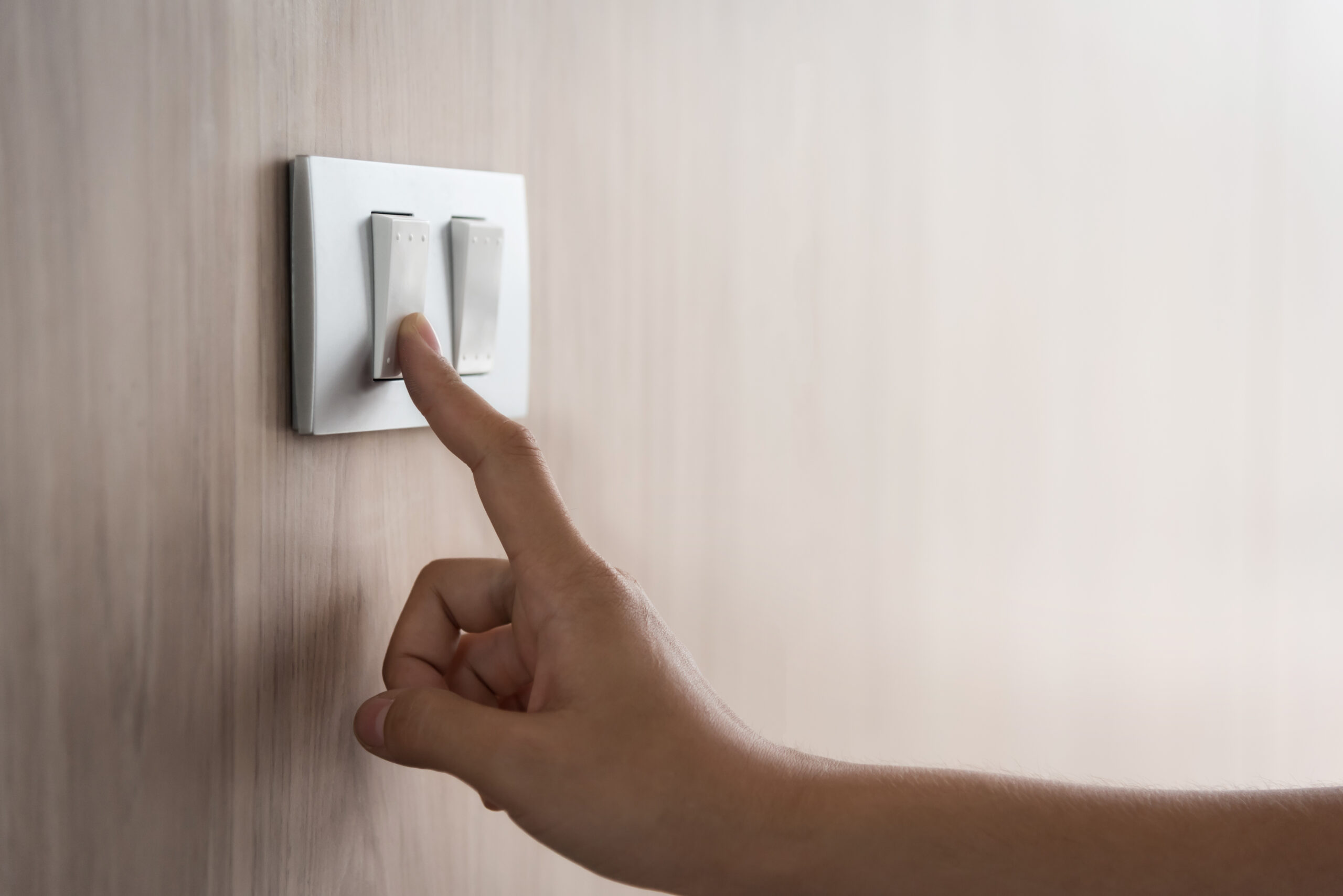 A hand is pointing to the light on a wall.