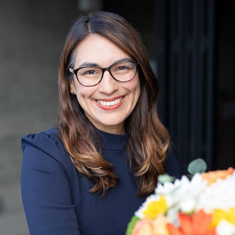 boardofdirectors—norena-limon A woman with glasses and a bouquet of flowers.