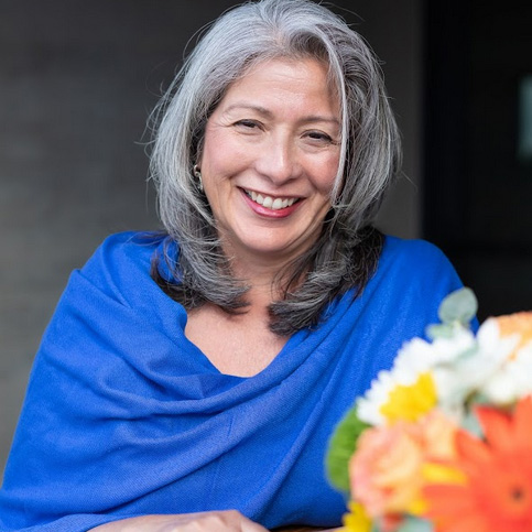 boardofdirectors—patricia-prado-olmoso A woman with gray hair sitting in front of flowers.