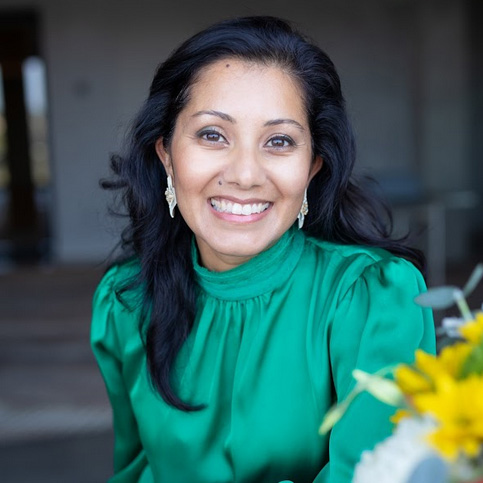 boardofdirectors—shreya-sasaki A woman in green shirt holding flowers and smiling.